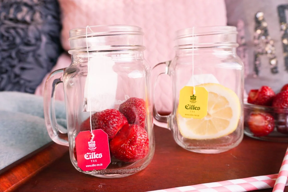 To glasskrus med håndtak, det ene fylt med jordbær og det andre med en sitronskive, begge med teposer merket "gillies iste.