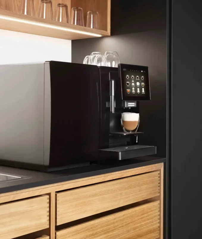 En moderne Franke A300 espressomaskin med digitalt display som serverer kaffe i en glasskopp, plassert i et elegant kjøkken med treskap og mørke vegger.