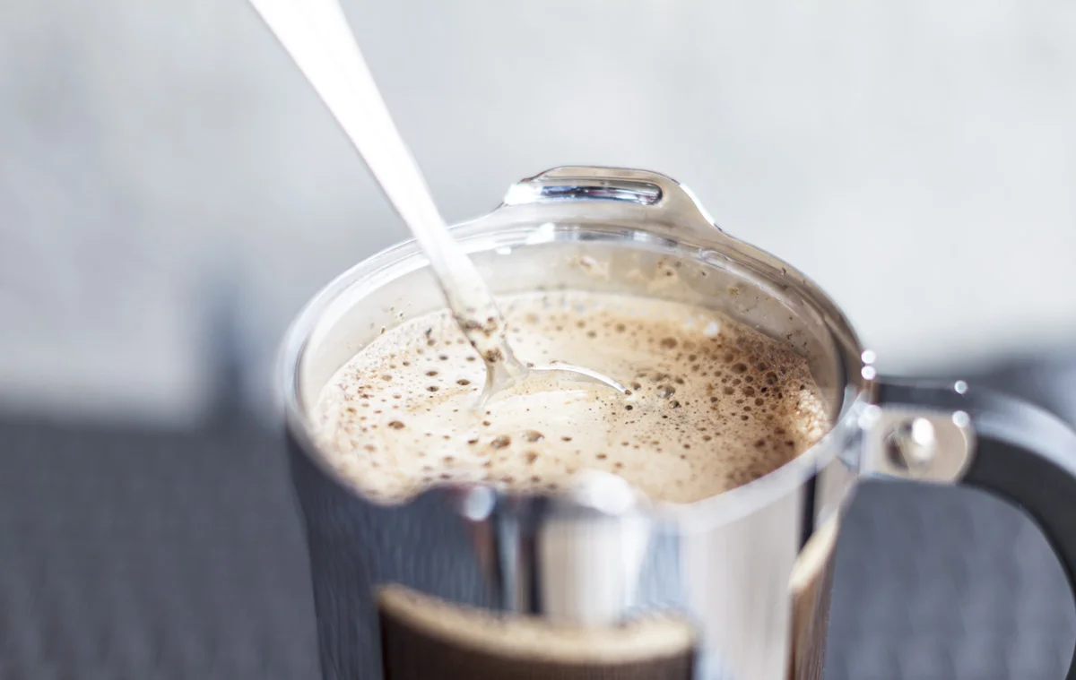 Melk helles i en presskannekaffe fylt med kaffe, og skaper bobler på overflaten.