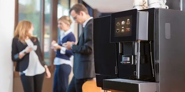 Franke A400 kaffemaskin i forgrunnen med tre uskarpe fagfolk som samtaler i bakgrunnen i kontormiljø.