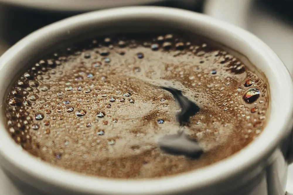 Nærbilde av en nytraktet kaffe fra en Rex Royal kompakt kaffemaskin i en hvit kopp, som viser detaljerte bobler og et virvlende mønster på overflaten.