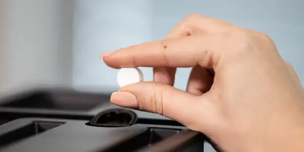 En persons hånd som plasserer en hvit rund pille i den beste kaffemaskin bedrift pillebeholderen.